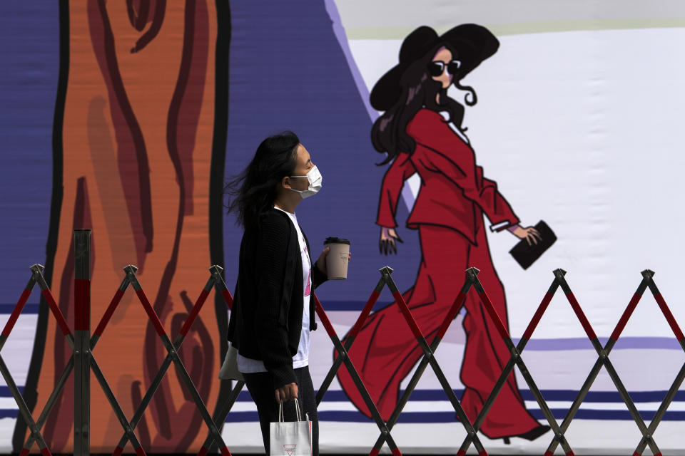 A woman wearing a face mask to help protect from the coronavirus walks by a barricaded construction wall displaying a fashion cartoon at a mall Sunday, April 24, 2022, in Beijing. Beijing is on alert after 10 middle school students tested positive for COVID-19, in what city officials said was an initial round of testing. (AP Photo/Andy Wong)