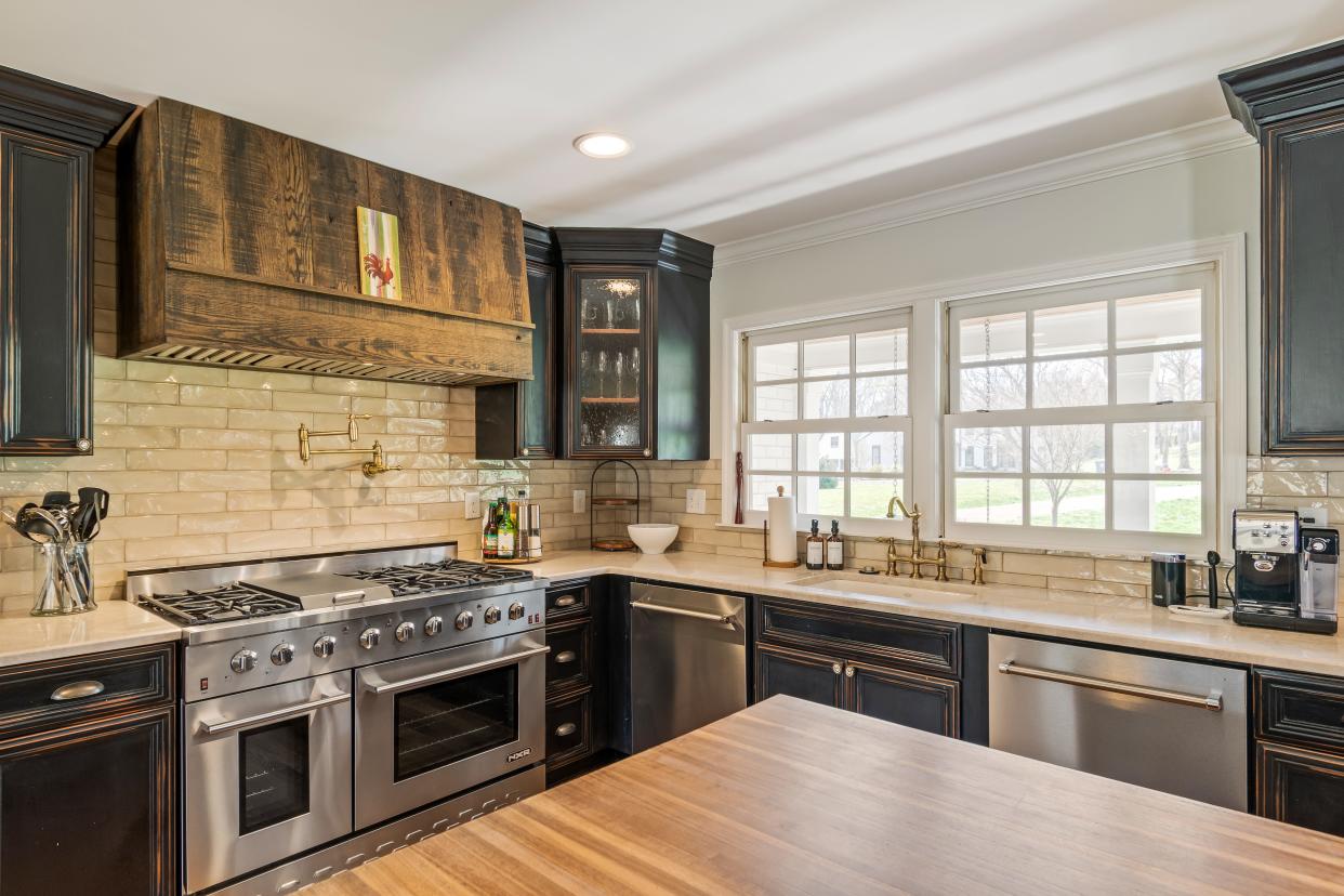 The farmhouse kitchen at 8202 Foxview Court features a large eat-at island, marble countertops, subway tile backsplash, and stainless appliances including a double oven and gas range.