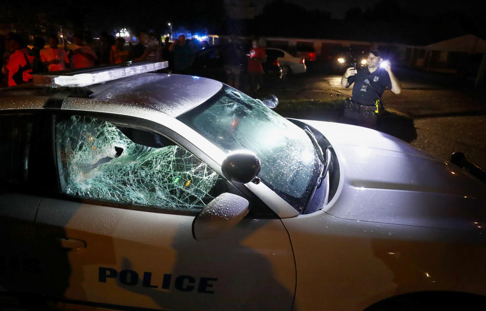 A Memphis police officer looks over a damaged squad car after protesters took to the streets of the Frayser community in anger against the shooting a youth by U.S. Marshals earlier in the evening, Wednesday, June 12, 2019, in Memphis, Tenn. Dozens of protesters clashed with law enforcement, throwing stones and tree limbs until authorities broke up the angry crowd with tear gas. (Mark Weber/Daily Memphian via AP)