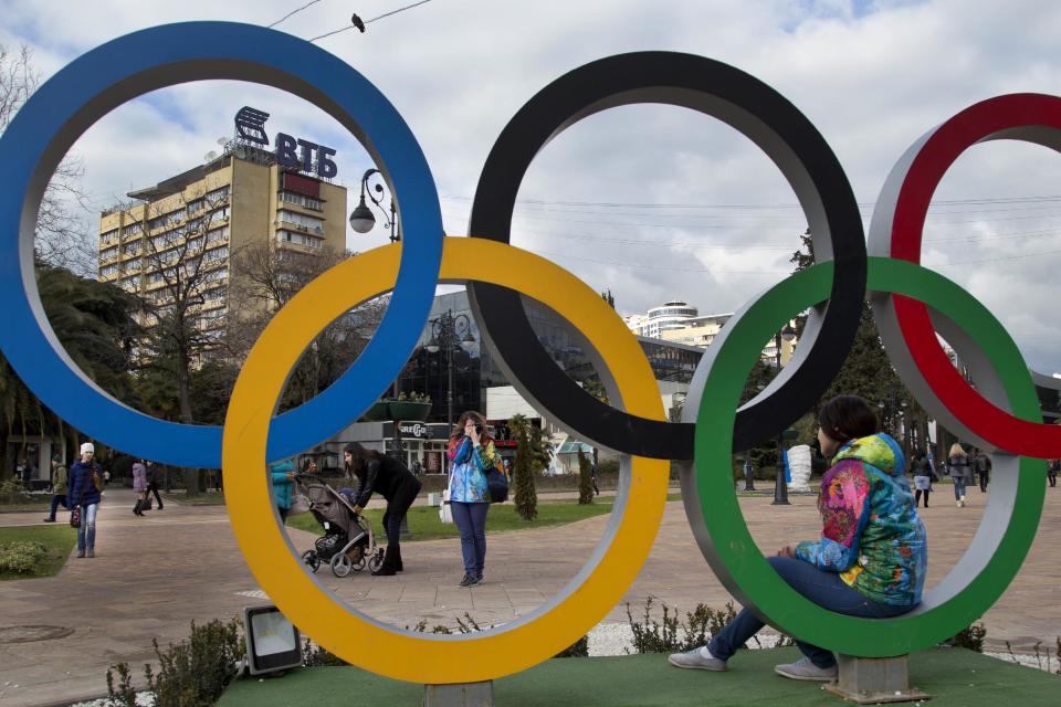 A Russian Olympic volunteer poses for snapshots next to the Olympic rings in Sochi, Russia, Tuesday, Feb. 4, 2014. The opening ceremony for the 2014 Winter Olympics will be held on Feb. 7. (AP Photo/Bernat Armangue)