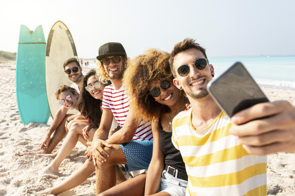 Friends sitting on the beach, having fun, taking selfies