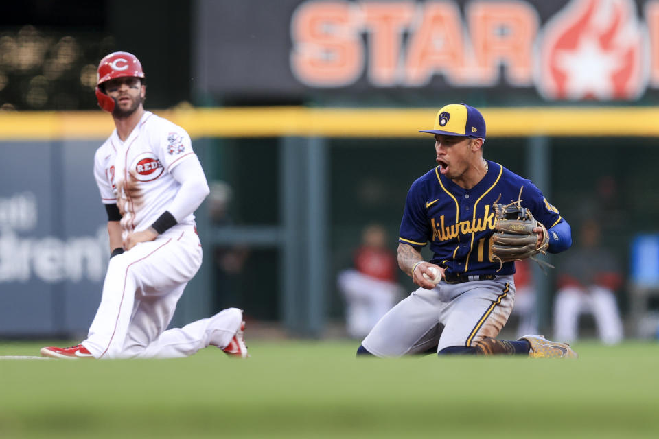 Milwaukee Brewers' Kolten Wong, right, reacts after he tagged out Cincinnati Reds' Tyler Naquin who was attempting to steal second base during the fourth inning of a baseball game in Cincinnati, Monday, May 9, 2022. (AP Photo/Aaron Doster)