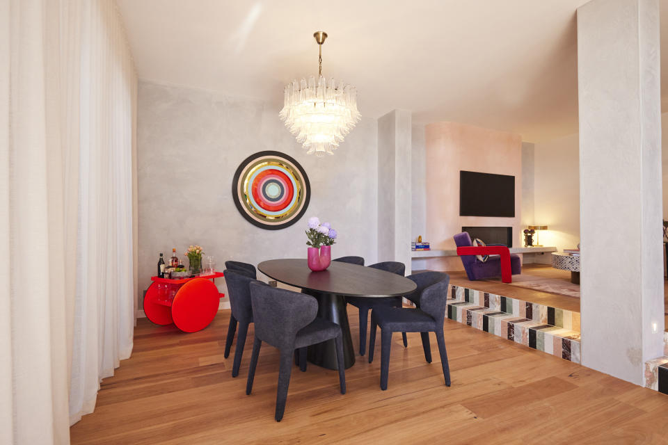 A wide shot of the dining room with the table in the centre, a red drinks cart and a circular artwork on the far wall.