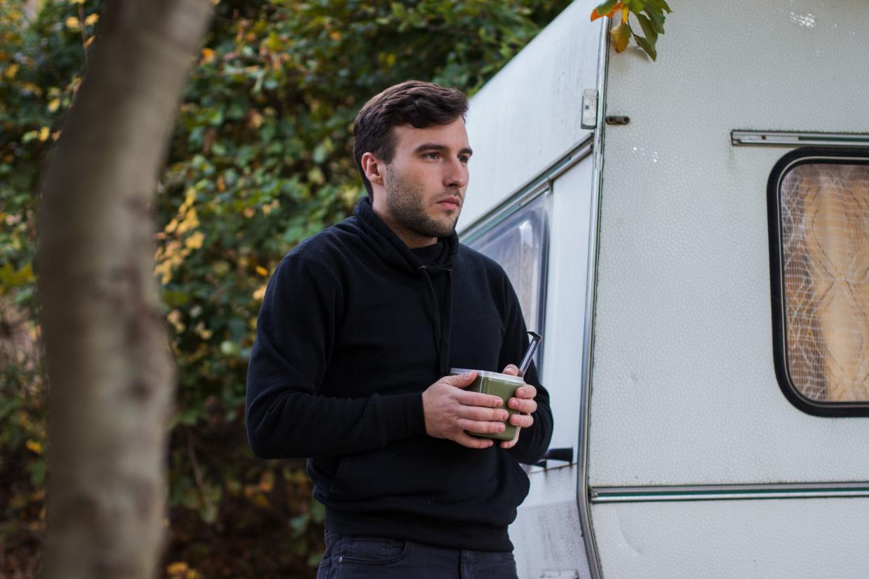 A young man stands in front of his camphouse