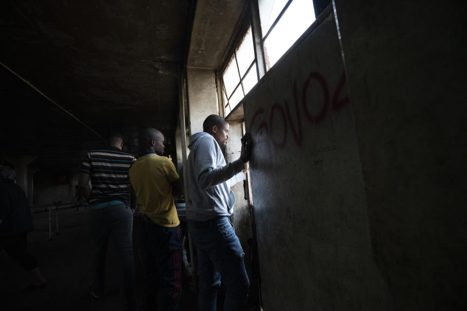 Residents of the Men's Hostel in the densely populated Alexandra township east of Johannesburg look at a deployment of South African National Defense Forces surrounding them Saturday, March 28, 2020. South Africa went into a nationwide lockdown for 21 days in an effort to control the spread of the COVID-19 coronavirus. The new coronavirus causes mild or moderate symptoms for most people, but for some, especially older adults and people with existing health problems, it can cause more severe illness or death. (AP Photo/Jerome Delay)