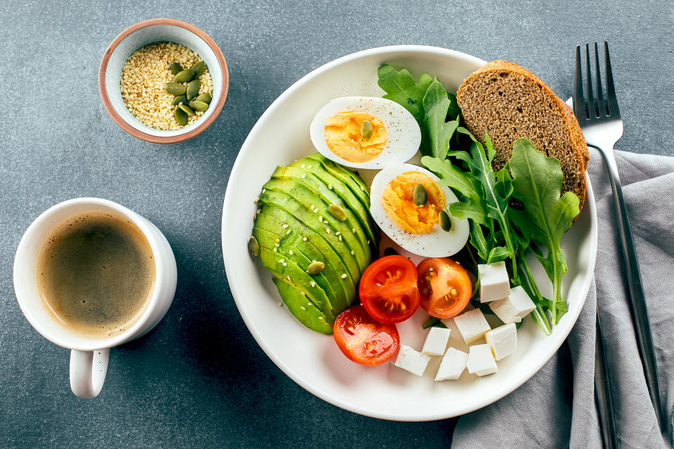 Healhty vegan breakfast bowl. Avocado, egg, tomato, feta cheese, arugula and bread and cup of coffee. Top view