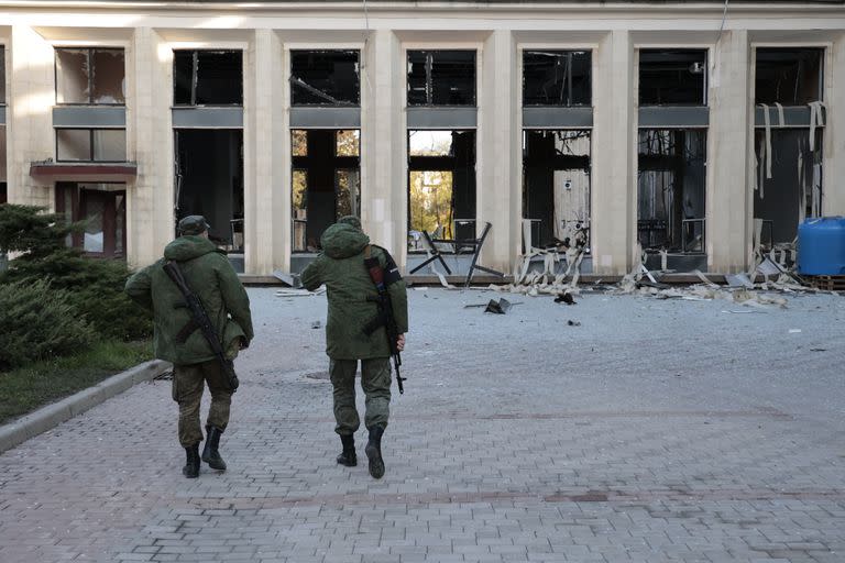 Dos militares armados caminan en el sitio de un edificio administrativo dañado después de un bombardeo en Donetsk, la capital de la República Popular de Donetsk, al este de Ucrania, el domingo 16 de octubre de 2022.