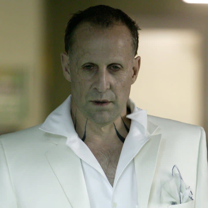 Stormare in a full white suit, tattoos on his neck, scarred face