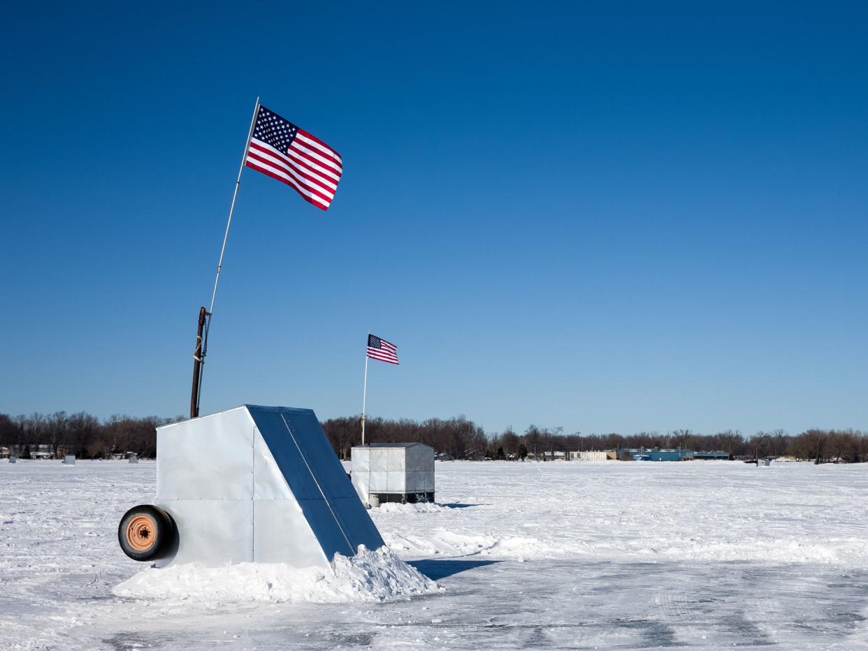 A pair of ice shanties on a frozen lake flying American flags. Copy space in the sky. Concepts could include fishing, patriotism, culture, winter, nature, and others.