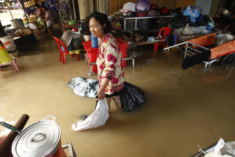 A woman continues to work in her home despite flooding from recent rains outside Phnom Penh , Cambodia, Wednesday, Oct. 14, 2020. A Cambodian disaster official said Wednesday that more than 10,000 people have been evacuated to the safety places after the tropical storm hit the country by causing the flash flood. (AP Photo/Heng Sinith)