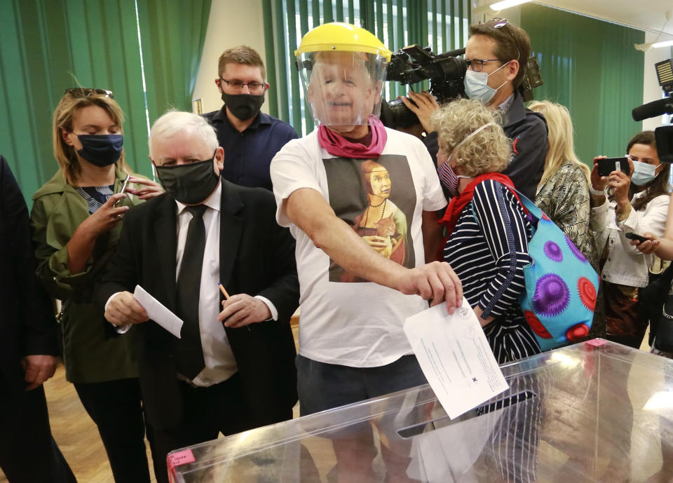 Leader of Poland's right-wing ruling party Jaroslaw Kaczynski, left, wearing a face mask for protection against the coronavirus, casts his ballot in tight presidential election runoff in Warsaw, Poland, on Sunday, July 12, 2020, next to a man wearing a face mask of Kaczynski's likeness. The ruling Law and Justice party is backing the reelection bid of incumbent conservative President Andrzej Duda, against the liberal Warsaw Mayor Rafal Trzaskowski. Latest opinion polls suggested that the runoff will be decided by a very narrow margin. (AP Photo)