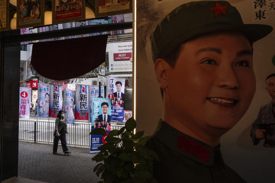 A poster featuring a performer dressed as former Chinese leader Mao Zedong at a Cantonese opera theatre is seen as a pedestrian walks past posters promoting candidates during the District Council elections in Hong Kong, Sunday, Dec. 10, 2023. Residents went to the polls on Sunday in Hong Kong's first district council elections since an electoral overhaul was implemented under Beijing's guidance of “patriots” administering the city, effectively shutting out all pro-democracy candidates. (AP Photo/Louise Delmotte)