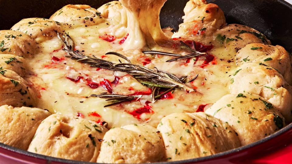 brie dip in a cast iron skillet swirled with cranberry sauce and surrounded by herby biscuits