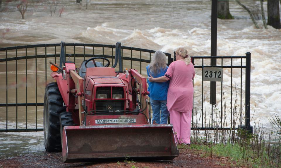 Kathy Covington, center, watches the powerful floodwaters of the Pearl River rush through her Florence, Miss., yard on Feb. 16, 2020.