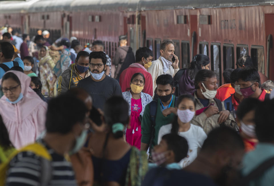 Passengers arrive wearing face masks at a train station in Mumbai, India, Thursday, Dec 23, 2021. The government on Thursday in a review meeting cautioned states to observe all precautions and don't let the guard down in view of the rise in Omicron variant cases. (AP Photo/Rafiq Maqbool)