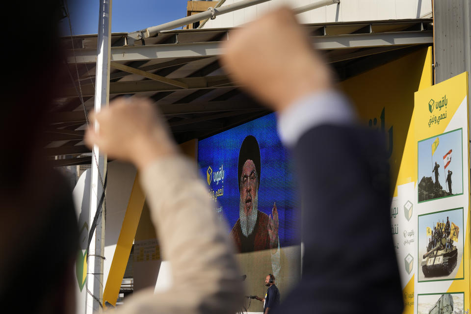 Hezbollah supporters raise their fists and cheer, as they listens to a speech by Hezbollah leader Sayyed Hassan Nasrallah through a giant screen during an election campaign, in the southern suburb of Beirut, Lebanon, Tuesday, May 10, 2022. Despite a devastating economic collapse and multiple other crises gripping Lebanon, the culmination of decades of corruption and mismanagement, the deeply divisive issue of Hezbollah's weapons has been at the center of Sunday's vote for a new 128-member parliament. (AP Photo/Hussein Malla)