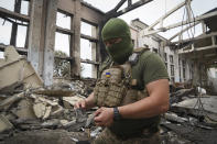 A Ukrainian serviceman holds rocket fragments at the ruins of the sports complex of the National Technical University in Kharkiv, Ukraine, Friday, June 24, 2022, damaged during a night shelling. The building received significant damage. A fire broke out in one part but firefighters managed to put it out. (AP Photo/Andrii Marienko)