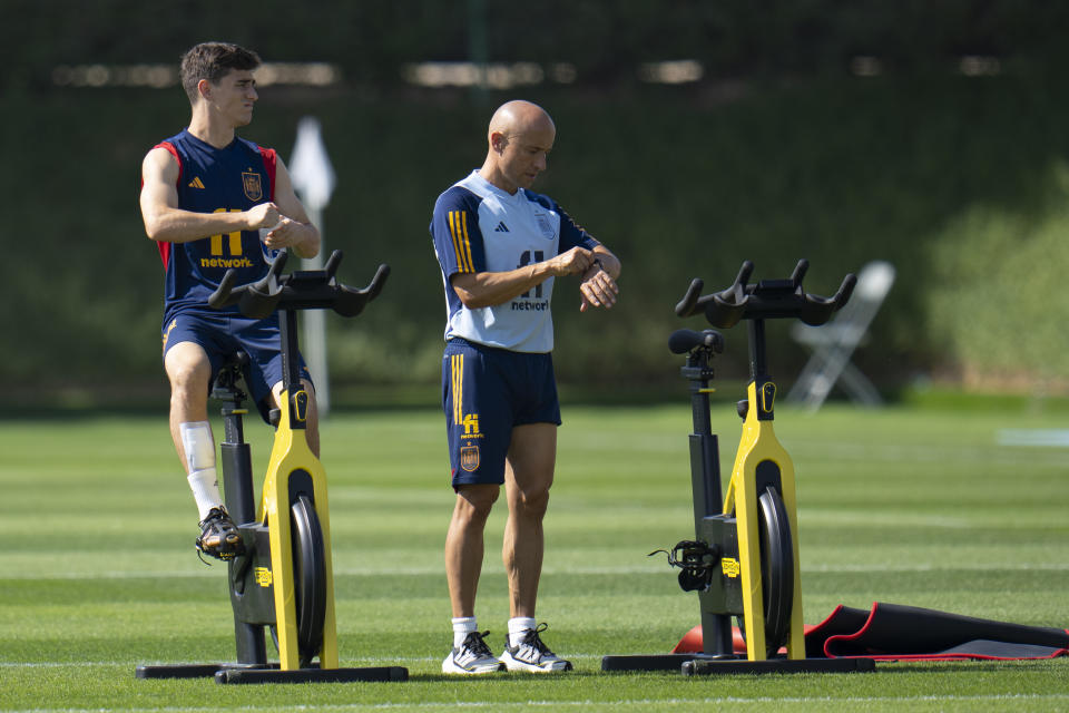 Spain's Gavi, left, works out on a stationary bike next to trainer Lorenzo del Pozo during a training session at Qatar University, in Doha, Qatar, Tuesday, Nov. 29, 2022. Spain will play its first final match in Group E in the World Cup against Japan on Dec. 1. (AP Photo/Julio Cortez)