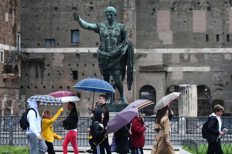 People walk past the statue of Emperor Augustus on a rainy day in Rome