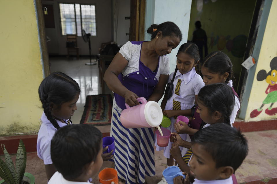 Primary students receive a cup of fresh milk at a Primary School in Dimbulagala, about 200 kilometres north east of Colombo, Sri Lanka, Monday, Dec. 12, 2022. Due to Sri Lanka's current economic crisis in Dimbulagala primary school children receive a free breakfast, a glass of milk and lunch with help from the education ministry, WFP and a private donor agency. Mothers of students prepare the meals at school with the menu provided by the education ministry. Each meal costs $0.27. (AP Photo/Eranga Jayawardena)