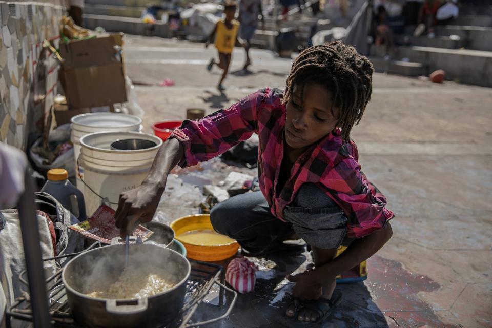 A woman stirs a pot of food at the Hugo Chavez public square transformed into a refuge for families forced to leave their homes due to clashes between armed gangs in Port-au-Prince, Haiti, Thursday, Oct. 20, 2022. (AP Photo/Odelyn Joseph)