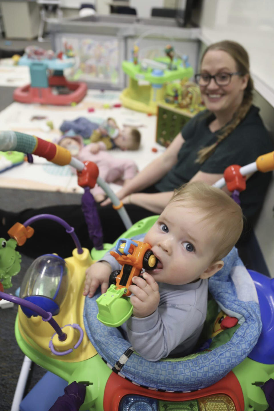 An infant plays with a toy at Endeavor Elementary's onsite daycare as former second grade teacher at the school, Billi Clark, back, watches over on Feb. 29, 2024, in Nampa, Idaho. Clark now runs the daycare. (Carly Flandro/Idaho Education News via AP)