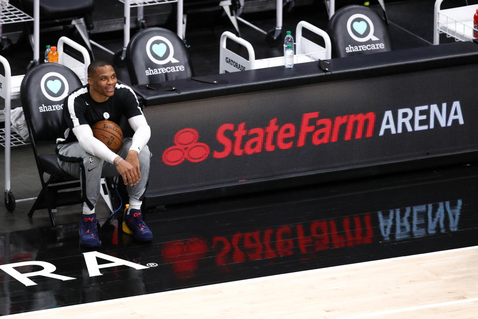Russell Westbrook smiles while sitting on the bench holding a basketball during pregame warmups. 