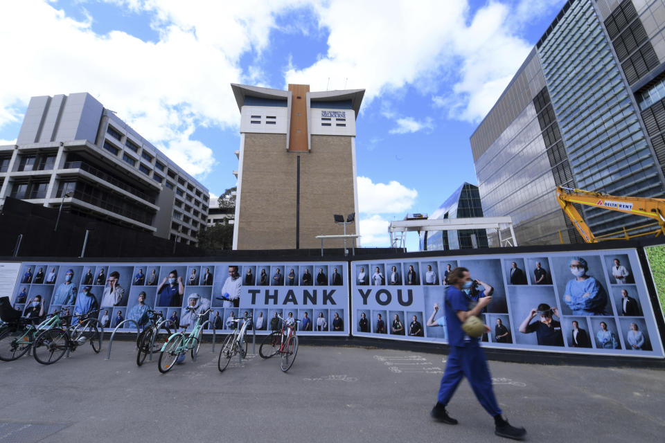 A man wearing a face mask walks past an outdoor photography exhibition of healthcare workers in Melbourne, Tuesday, Sept. 22, 2020. The photo essay created by photographer Phoebe Powell is to acknowledge the people working in the Parkville Biomedical Precinct which is home to some of the world's leading medical researchers, clinicians and academics keeping Victoria state safe during the coronavirus pandemic. (James Ross/AAP Image via AP)