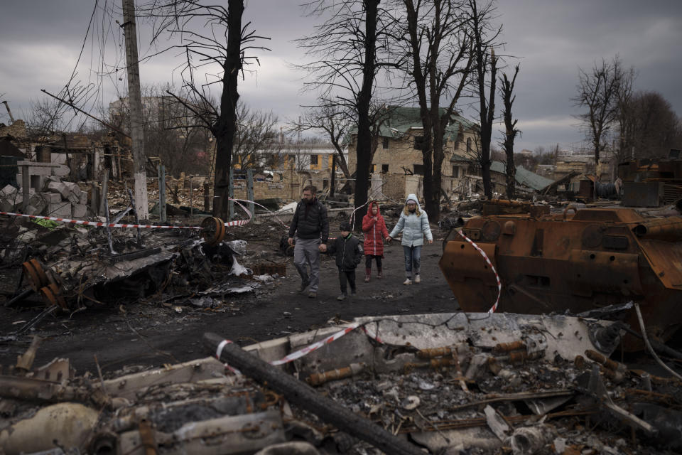 FILE - A family walks amid destroyed Russian tanks in Bucha, on the outskirts of Kyiv, Ukraine, Wednesday, April 6, 2022. (AP Photo/Felipe Dana, File)