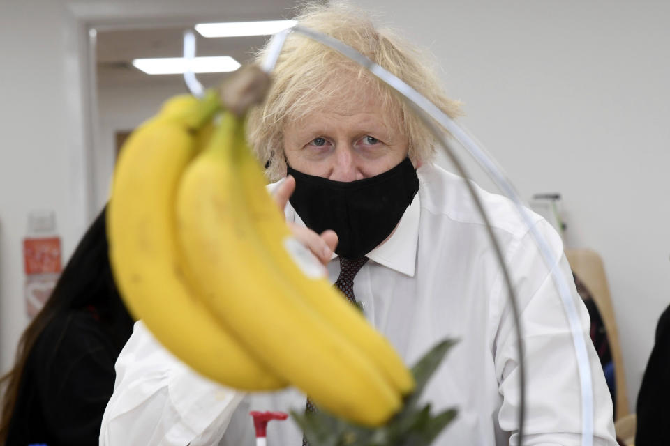British Prime Minister Boris Johnson looks at a bunch of bananas to draw during a visit to the Monkey Puzzle Nursery in Greenford, west London, Thursday, March 25, 2021. (Jeremy Selwyn/Pool Photo via AP)