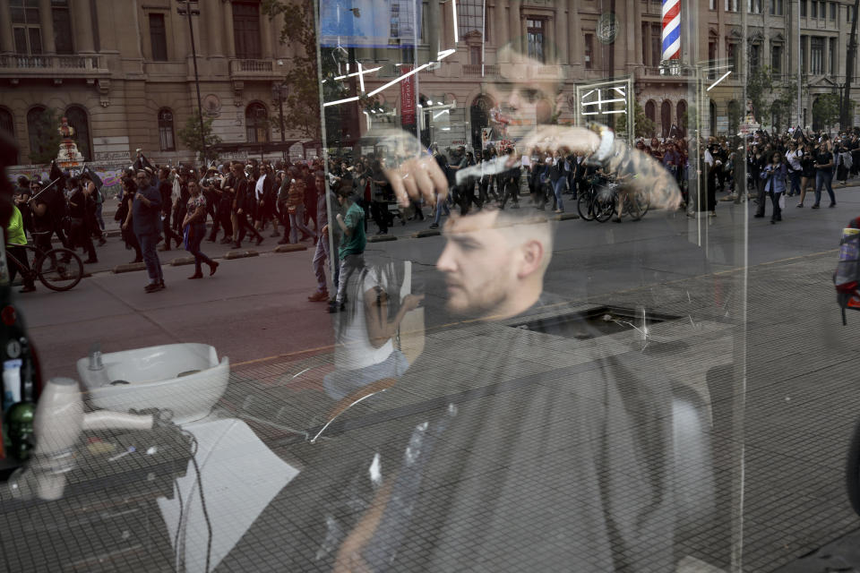 Anti-government demonstrators are reflected in the window of a hairdressing salon in Santiago, Chile, Friday, Nov. 1, 2019. Groups of Chileans continued to protest as government and opposition leaders debated the response to nearly two weeks of protests that have paralyzed much of the capital and forced the cancellation of two major international summits. (AP Photo/Rodrigo Abd)