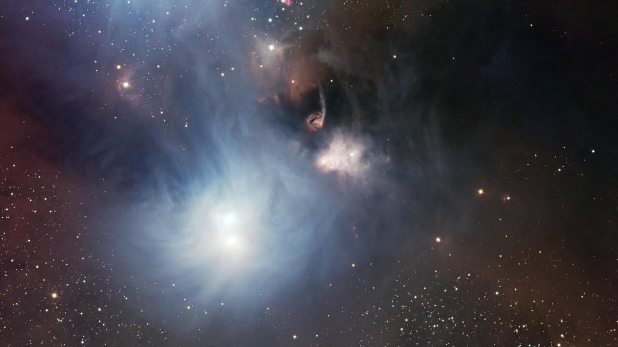  a telescopic view of wispy star-forming regions seen from afar. glowing stars puncture vast clouds of gas, scattered among stars 