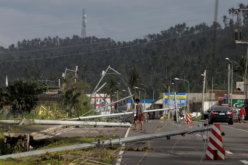 A man walks past electric poles lying on the main highway after Typhoon Kammuri hit Camalig town