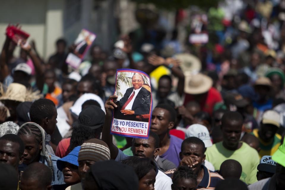 A demonstrator holds up a picture of Haiti's former President Jean-Bertrand Aristide, that reads in Creole "The more they persecute him, the more we love him", during a rally to mark the tenth anniversary of his second ouster in Port-au-Prince, Haiti, Thursday Feb. 27, 2014. The protesters denounced what they described as widespread corruption in the government of President Michel Martelly and even called for his resignation. (AP Photo/Dieu Nalio Chery)