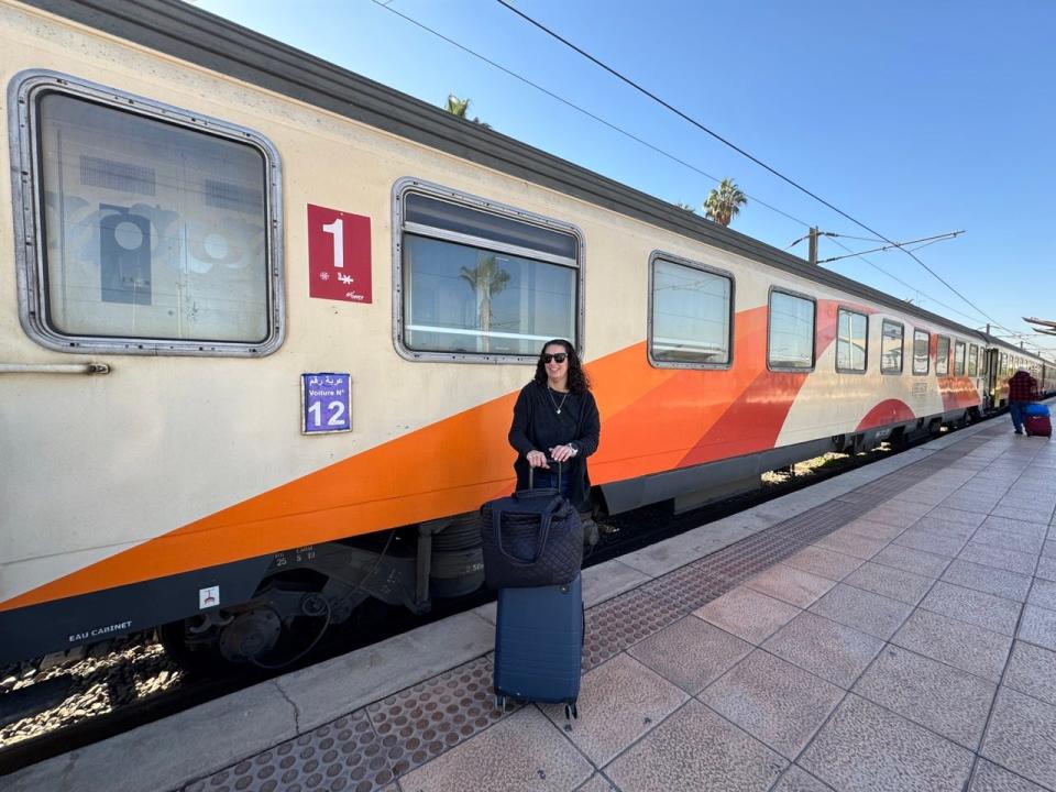 Author Jamie Davis Smith standing with suitcase next to train