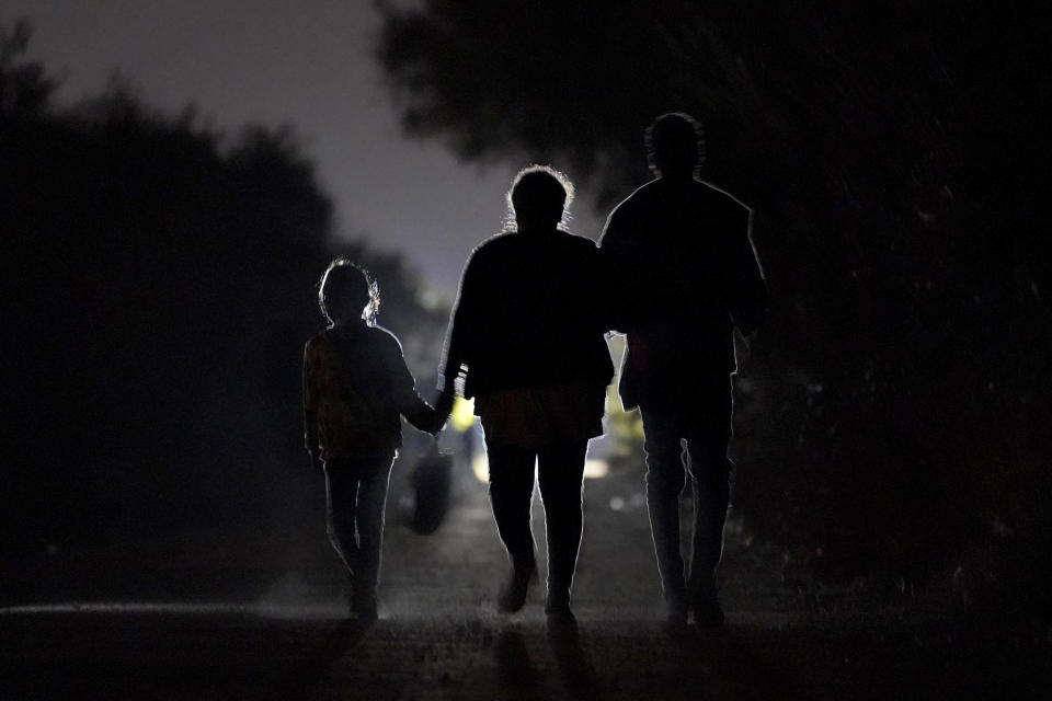 A 7-year-old migrant girl from Honduras, left, walks with Fernanda Solis, 25, center, also of Honduras, and an unidentified man as they approach a U.S. Customs and Border Protection processing center to turn themselves in while seeking asylum moments after crossing the U.S.-Mexico border, Sunday, March 21, 2021, in Mission, Texas. The girl's journey illustrates the extraordinary risks taken by parents to get their children across the border, even if it means abandoning them for the most perilous part of the trip. She is one of thousands of kids arriving alone in the U.S. in a surge that is straining the federal government's system for managing refugees. (AP Photo/Julio Cortez)