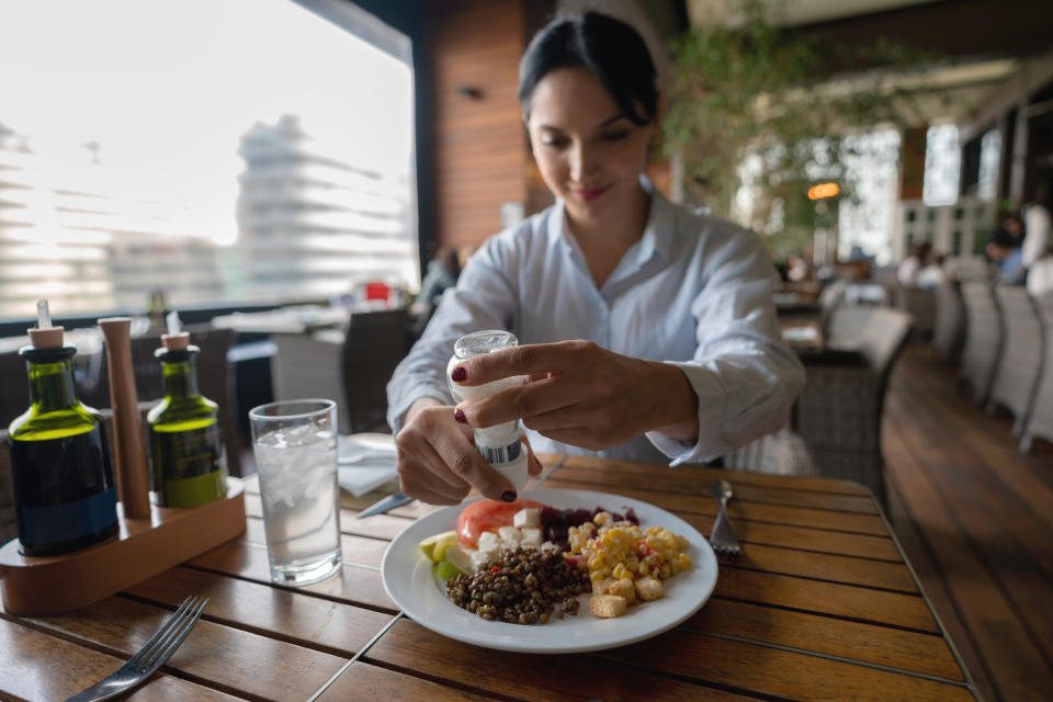 Latin american woman enjoying a healthy meal at the hotel restaurant seasoning her salad with salt