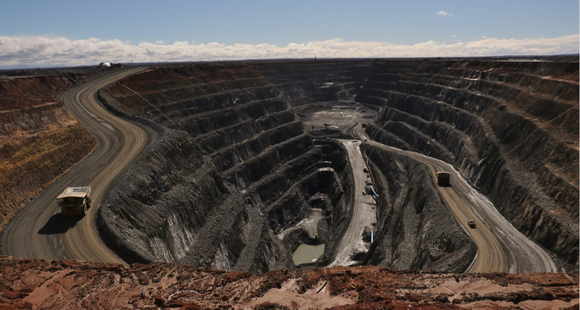 Open pit mine with trucks and other equipment running through it.