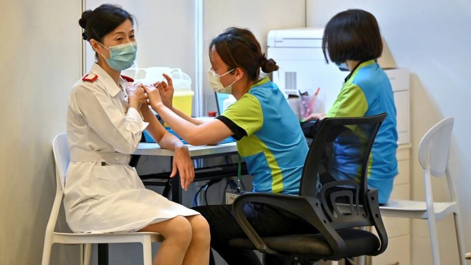 香港某社區疫苗接種中心內一位女護士（左）接受一位女工作人員（右）注射科興新冠病毒疫苗（23/2/2021）