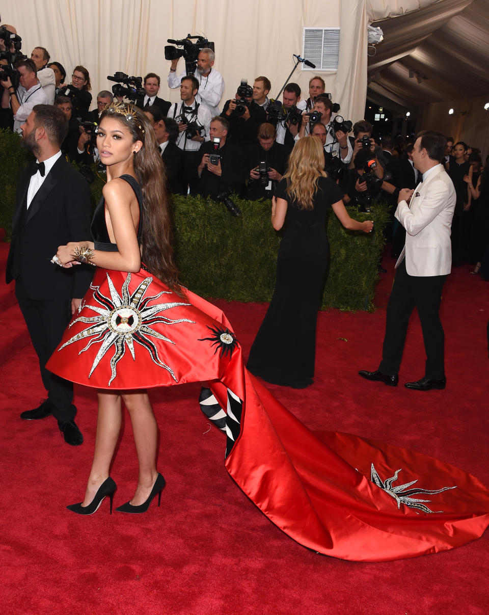 Woman in a dress with star and sun motifs on a long train, photographers in background