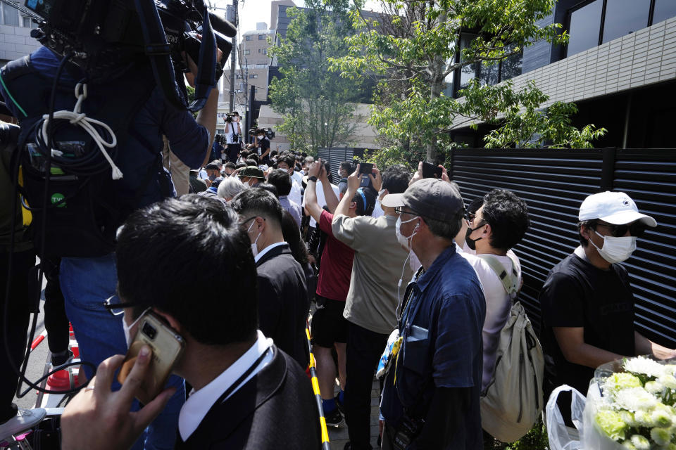 Pedestrians try to take snap shots as the media wait for the vehicle carrying the body of the former Prime Minister Shinzo Abe to arrive at his home in Tokyo, Saturday, July 9, 2022. Abe was shot Friday while delivering his speech to support the Liberal Democratic Party's candidate during an election campaign in Nara, western Japan. (AP Photo/Hiro Komae)