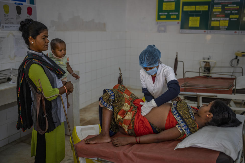 A nurse checks Phagni Poyam, 23, a nine months pregnant woman, as a health worker Basanti Warda, left, holds Poyam's one-year-old son Dilesh at a hospital in Orchha in central India's Chhattisgarh state, Nov. 16, 2022. These ambulances, first deployed in 2014, reach inaccessible villages to bring pregnant women to an early referral center, a building close to the hospital where expectant mothers can stay under observation, routinely visit doctors if needed until they give birth. Since then the number of babies born in hospitals has doubled to a yearly average of about 162 births each year, from just 76 in 2014. The state has one of the highest rates of pregnancy-related deaths for mothers in India, about 1.5 times the national average, with 137 pregnancy related deaths for mothers per 100,000 births. (AP Photo/Altaf Qadri)