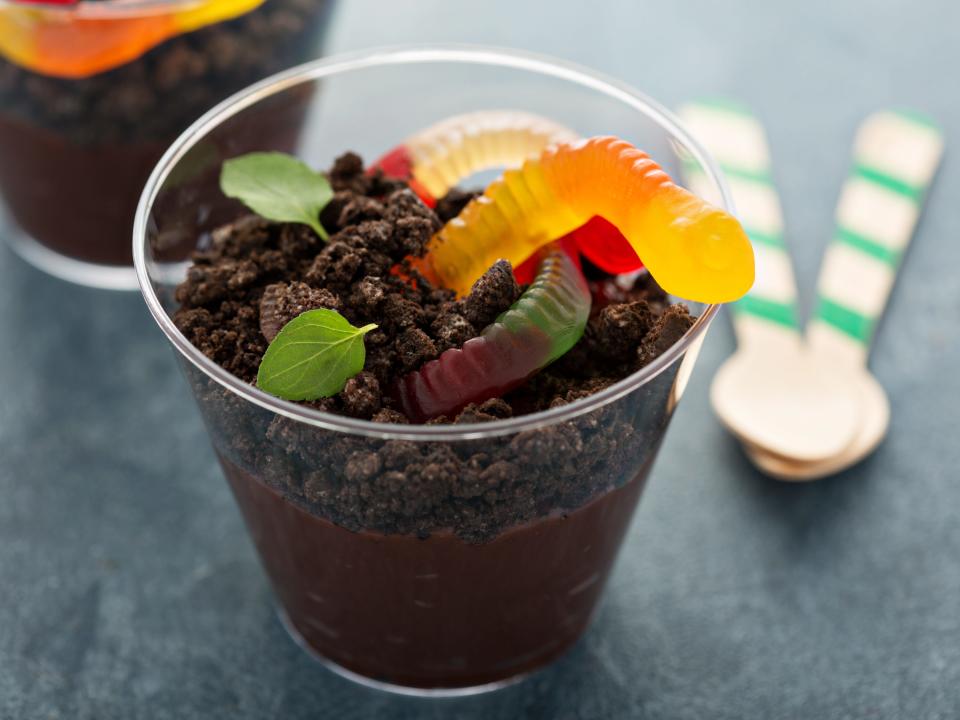a cup of chocolate pudding topped with crushed chocolate cookies and gummy worms for a Dirt and Worms dessert