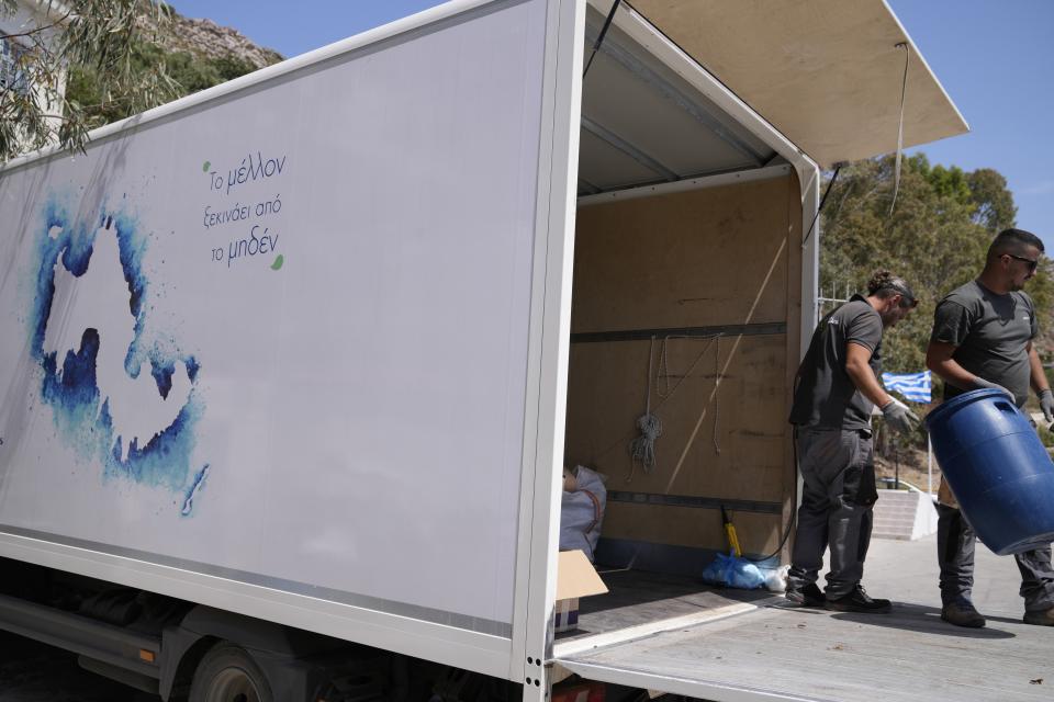 Waste collection crew members load trash for recycling into a truck on the Aegean Sea island of Tilos, southeastern Greece, Monday, May 9, 2022. When deciding where to test green tech, Greek policymakers picked the remotest point on the map, tiny Tilos. Providing electricity and basic services, and even access by ferry is all a challenge for this island of just 500 year-round inhabitants. It's latest mission: Dealing with plastic. (AP Photo/Thanassis Stavrakis)