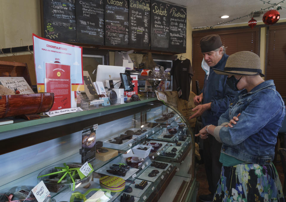 Jeffray Gardner, the owner of Marsatta Chocolate explains his artisan hand-crafted chocolates to new customer, Katherine Trontman at his company's flagship store in Torrance, Calif., Sunday, March 28, 2021. Restaurants and delivery companies remain uneasy partners, haggling over fees and struggling to make the service profitable for themselves and each other. Gardner says he probably loses money on the one or two delivery orders he gets each day. But he’s still happy to work with delivery companies because they help him reach a wider audience. (AP Photo/Damian Dovarganes)