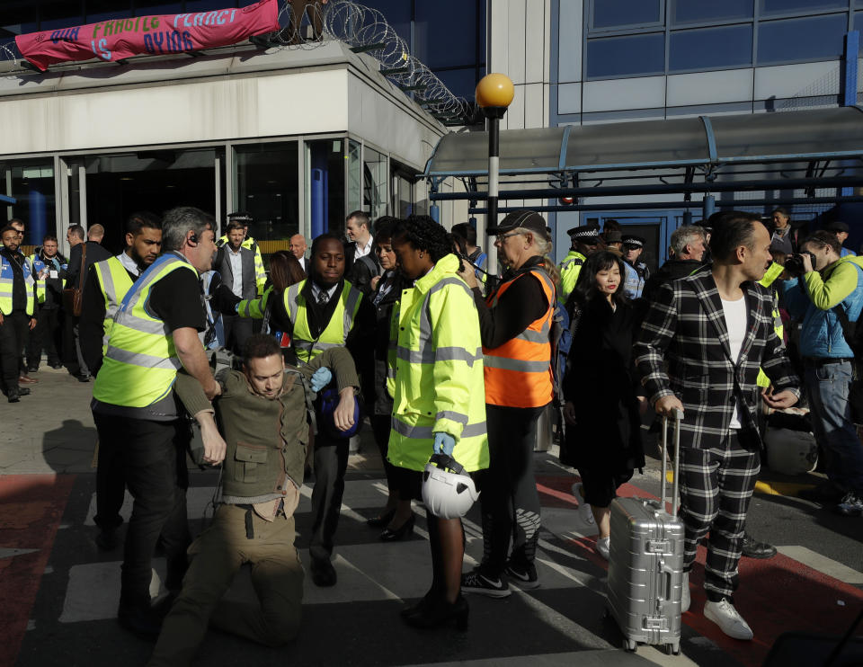 Travellers make their way past as an Extinction Rebellion demonstrator is removed at City Airport in London, Thursday, Oct. 10, 2019. Some hundreds of climate change activists are in London during a fourth day of world protests by the Extinction Rebellion movement to demand more urgent actions to counter global warming. (AP Photo/Matt Dunham)