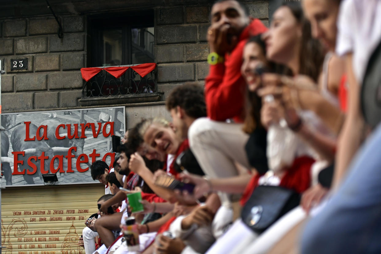 People sit on wooden barriers to watch the running of the bulls by the famous Estafeta curve on the first day at the San Fermin Festival in Pamplona, northern Spain, Thursday, July 7, 2022. Revellers from around the world flock to Pamplona every year for nine days of uninterrupted partying in Pamplona's famed running of the bulls festival which was suspended for the past two years because of the coronavirus pandemic. (AP Photo/Alvaro Barrientos)