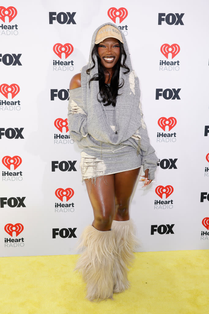 Woman in a hoodie dress and fluffy boots posing on yellow carpet with iHeartRadio and Fox logos in background