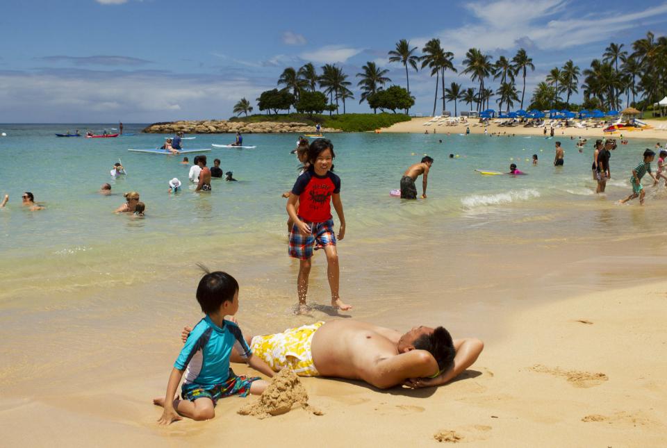 Two kids play with their dad on the beach as two hurricanes approach the Hawaiian islands, in Honolulu, Hawaii, August 6, 2014. Hawaiians braced for a one-two punch from a pair of major storms headed their way on Wednesday, as Hurricane Iselle bore down on the islands packing high winds and heavy surf and Julio, tracking right behind, was upgraded to hurricane status. REUTERS/Hugh Gentry (UNITED STATES - Tags: ENVIRONMENT DISASTER SOCIETY)