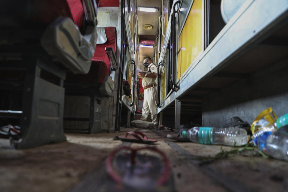 Sandals and water bottles lie scattered as a police officer inspects the interior of a parked bus onto which a truck struck overnight in Barabanki, Uttar Pradesh state, India, Wednesday, July 28, 2021. Police say a truck struck a group of laborers sleeping under the parked bus on the side of a highway in northern India, killing more than a dozen of them. (AP Photo/Sumit Kumar)